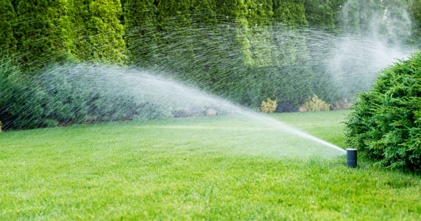 Technician fine-tuning sprinkler spray pattern near sloped lawn and retaining wall