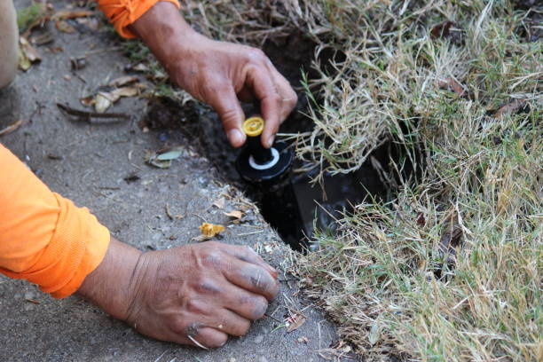 Technician fixing broken sprinkler head beside driveway edge and lawn border, Technician diagnosing leaking sprinkler valve in front yard near Salt Lake City sidewalk